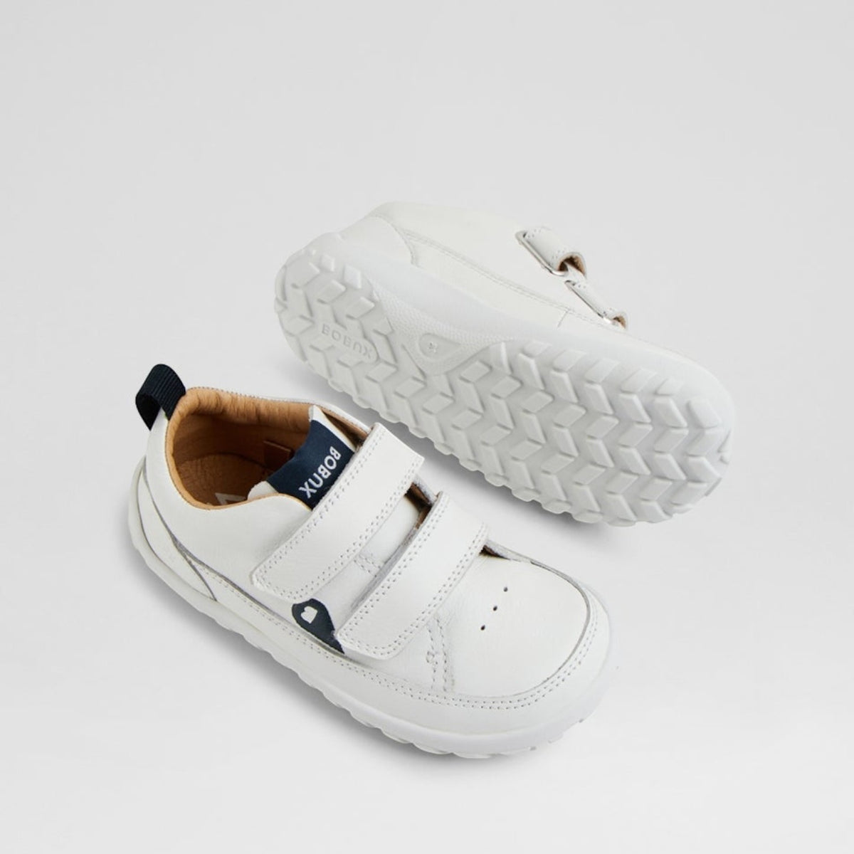 Baby sneakers by Bobux in white and navy, featuring soft soles and breathable fabric for comfortable little feet.