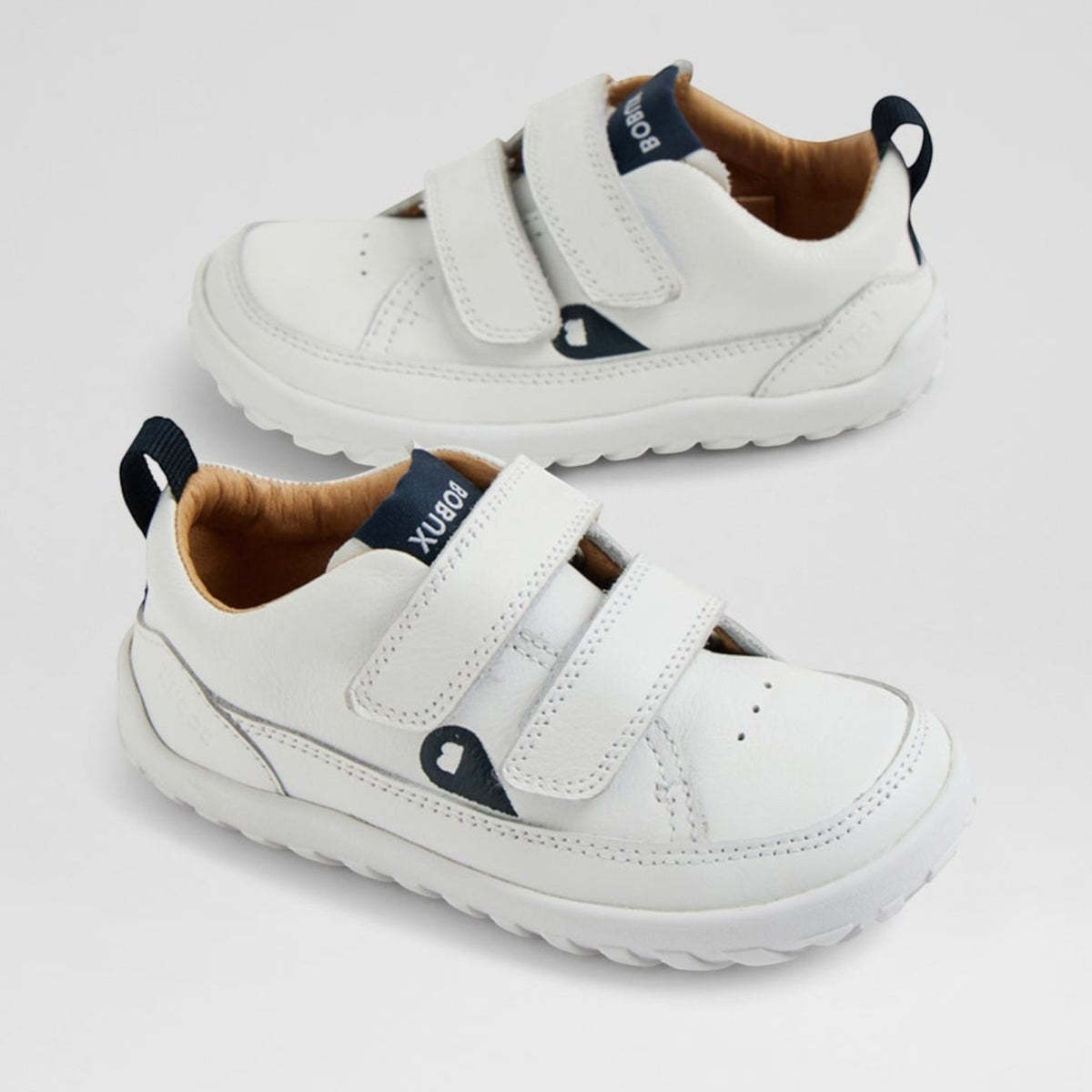 Baby sneakers in white and navy by Bobux, featuring soft soles and breathable material for comfortable infant footwear.