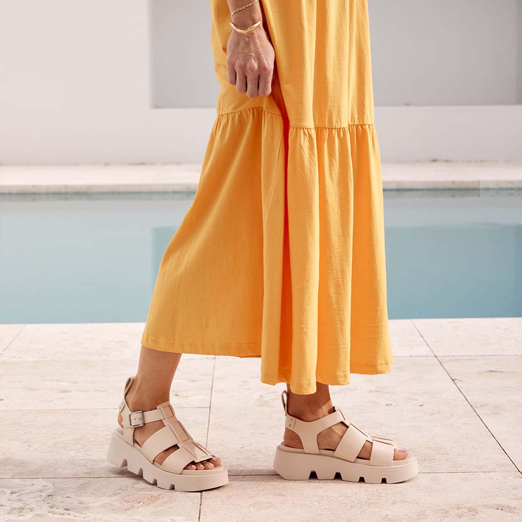 EOS KAILAN BONE sandals in beige with ankle straps and flat soles, displayed on a neutral background.
