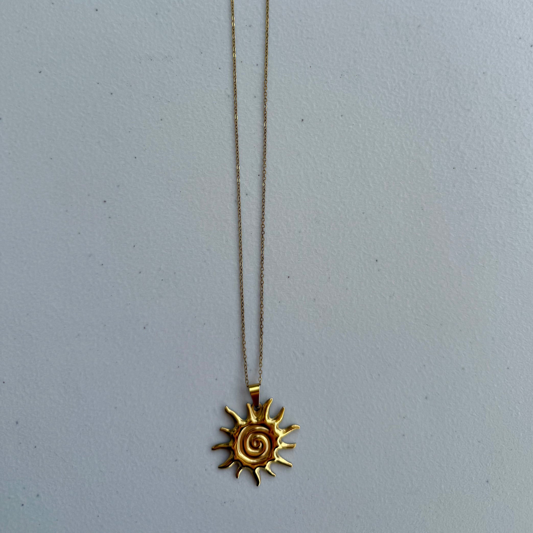 Gold spiral sun pendant necklace from Zeke Collection featuring a sleek, circular sun design on a delicate chain.