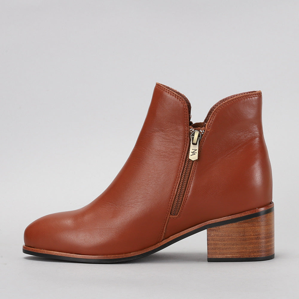 Naked Arches Oxley Cognac boots featuring smooth leather and stylish ankle design, laid on a wooden surface.