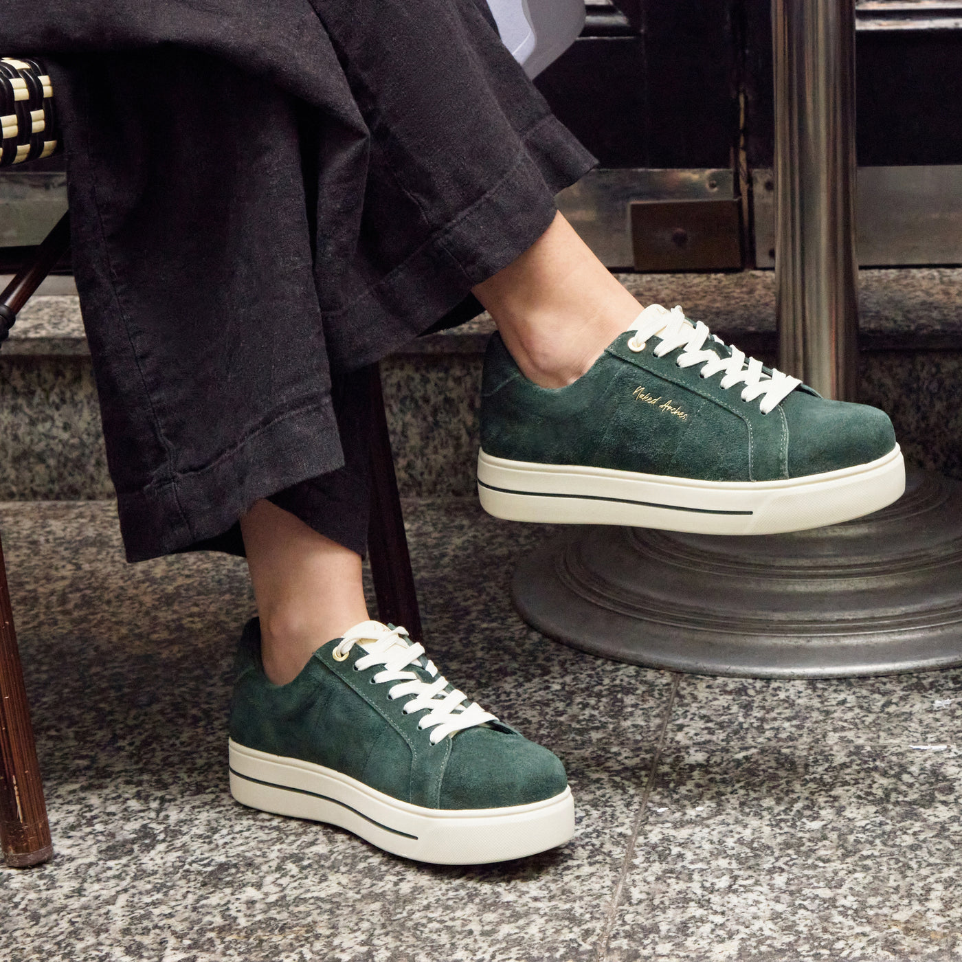 Naked Arches Azealia DK Green sneakers with sleek design, featuring green and black color accents, on a winter-themed background.