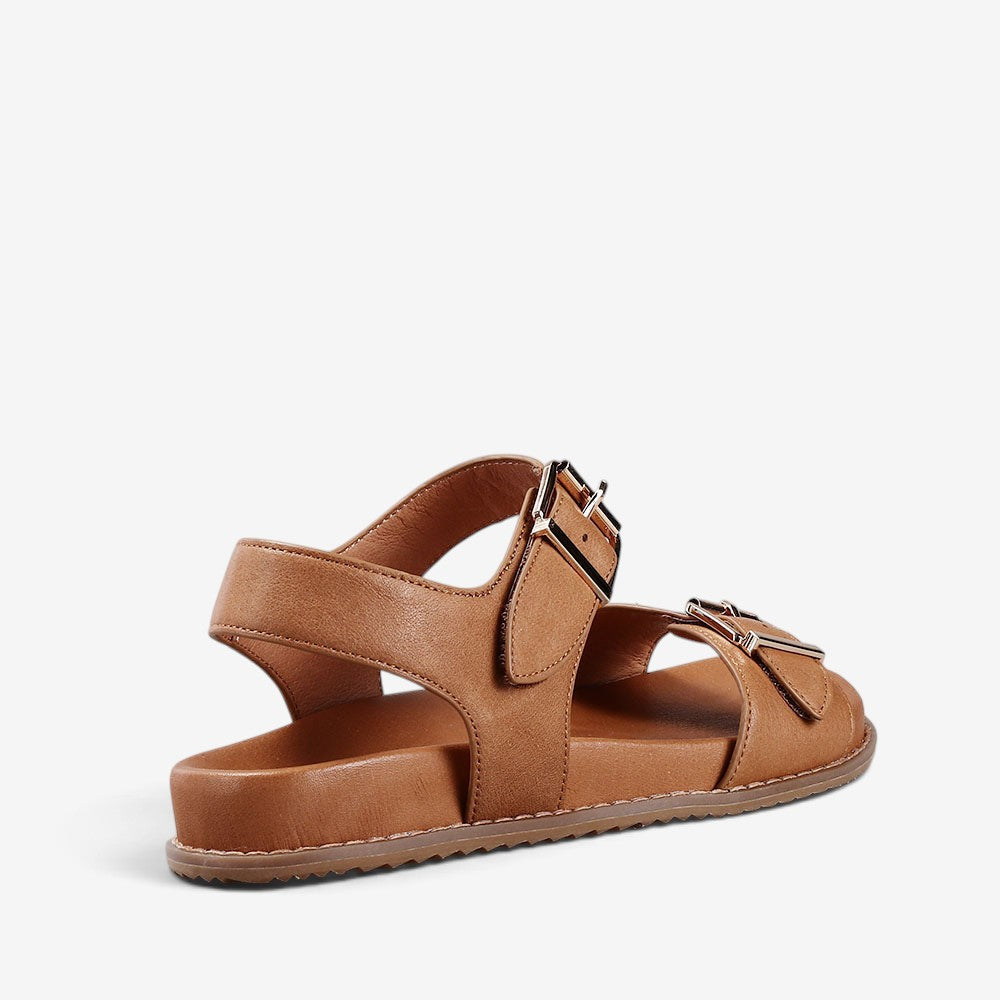 Naked Arches Ziggro Tan sandals with tan leather straps and flat sole, displayed on a neutral background.