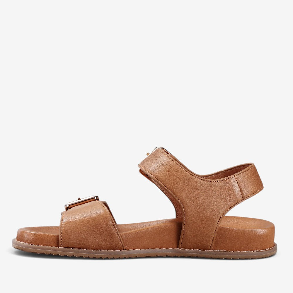 Naked Arches Ziggro Tan sandals featuring natural leather straps and a flat sole, displayed on a neutral background.